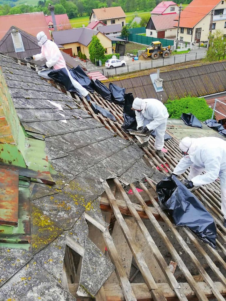Pracovníci v ochranných odevoch odstraňujú azbestovú krytinu